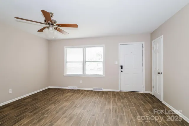 an empty room with wooden floor fan and windows