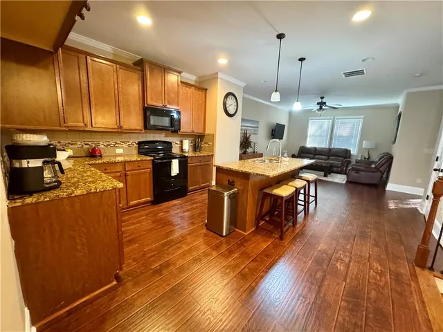 a kitchen with stainless steel appliances kitchen island granite countertop a stove a refrigerator a sink a dining table and chairs with wooden floor