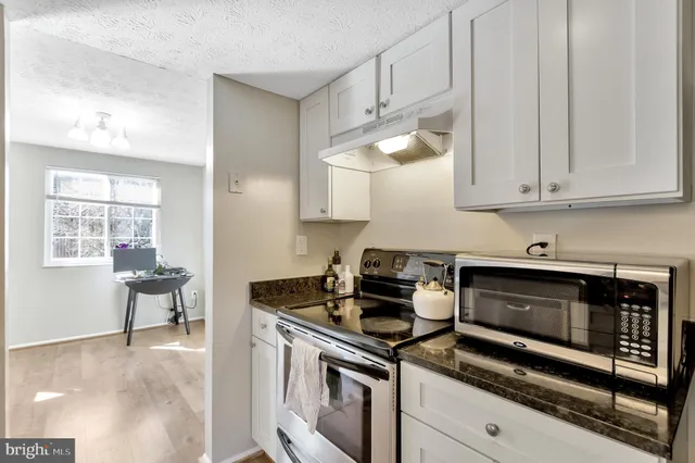 a kitchen with stainless steel appliances granite countertop white cabinets and a stove top oven