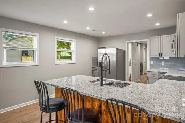 a kitchen with stainless steel appliances granite countertop a sink a stove a dining table and chairs