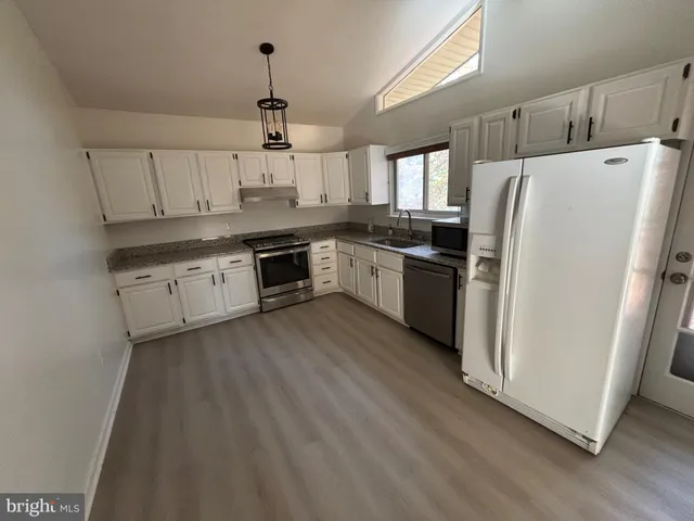 a kitchen with granite countertop a refrigerator a sink dishwasher a stove and white cabinets with wooden floor