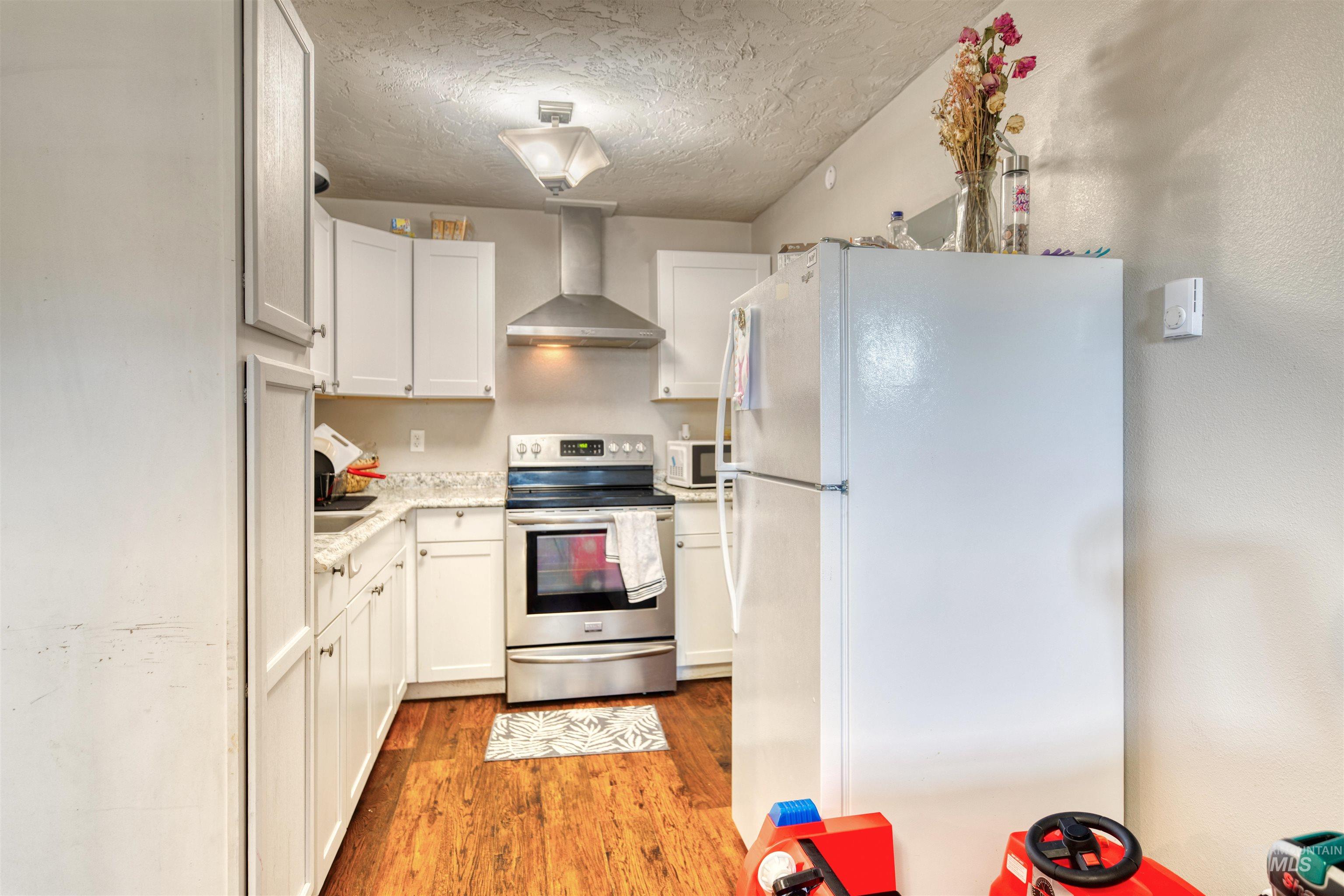 106 East Main Street Nyssa, OR 97913 - Photo 4 of 32 Kitchen featuring white appliances, wall chimney exhaust hood, light wood-type flooring, white cabinetry, and a textured ceiling
