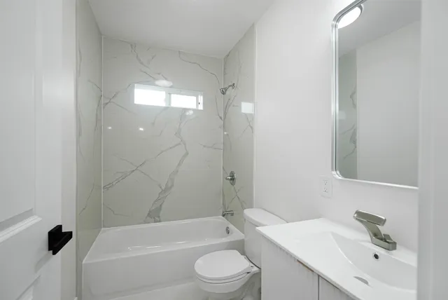 a bathroom with a bathtub shower sink vanity mirror and toilet