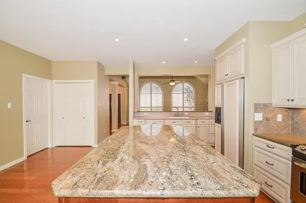 a large white kitchen with granite countertop a refrigerator and cabinets