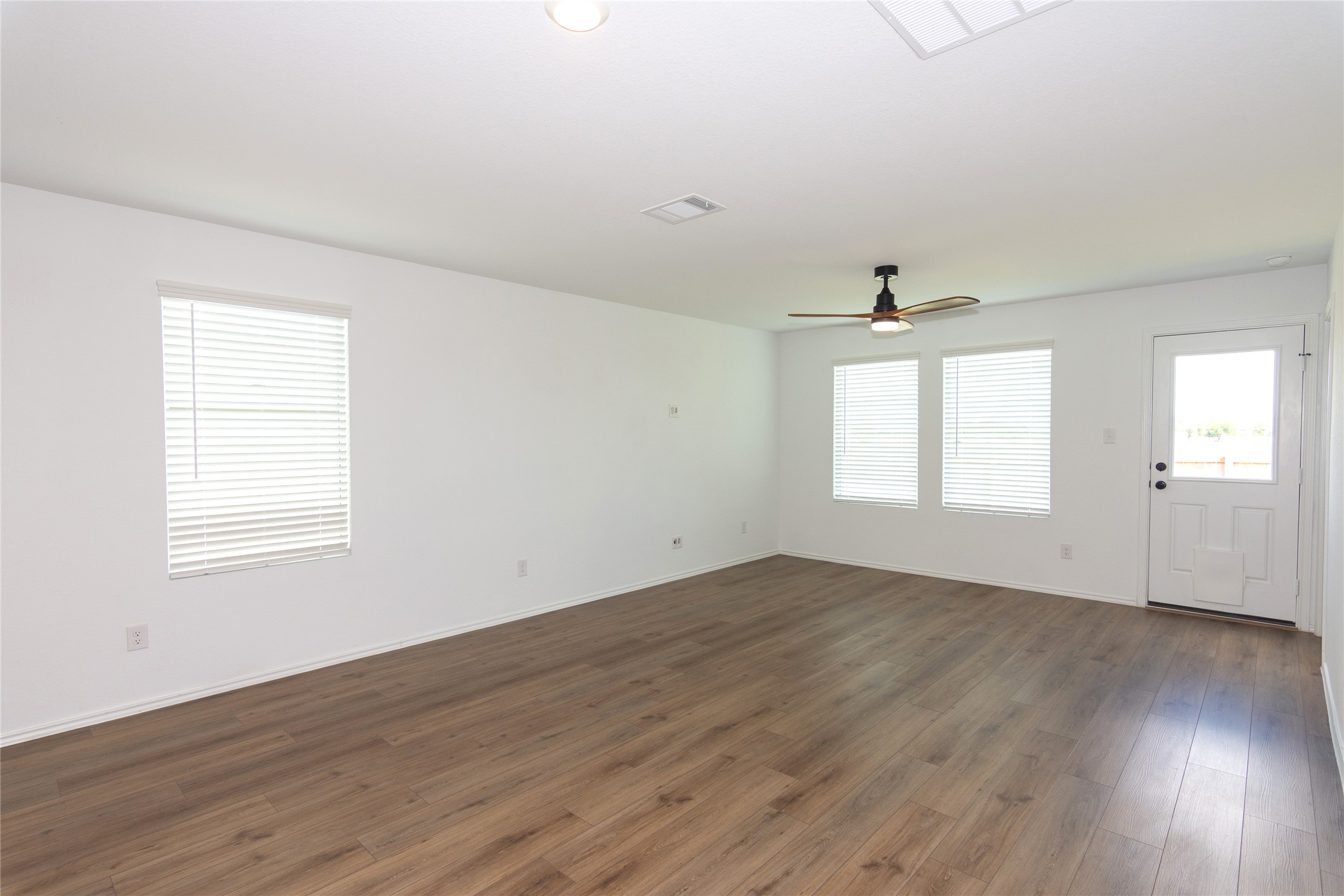 548 Rancho Del Cielo Loop Jarrell, TX 76537 - Photo 11 of 40 Expansive living room featuring wood-finish flooring, multiple windows with blinds, a ceiling fan, and a rear exterior door