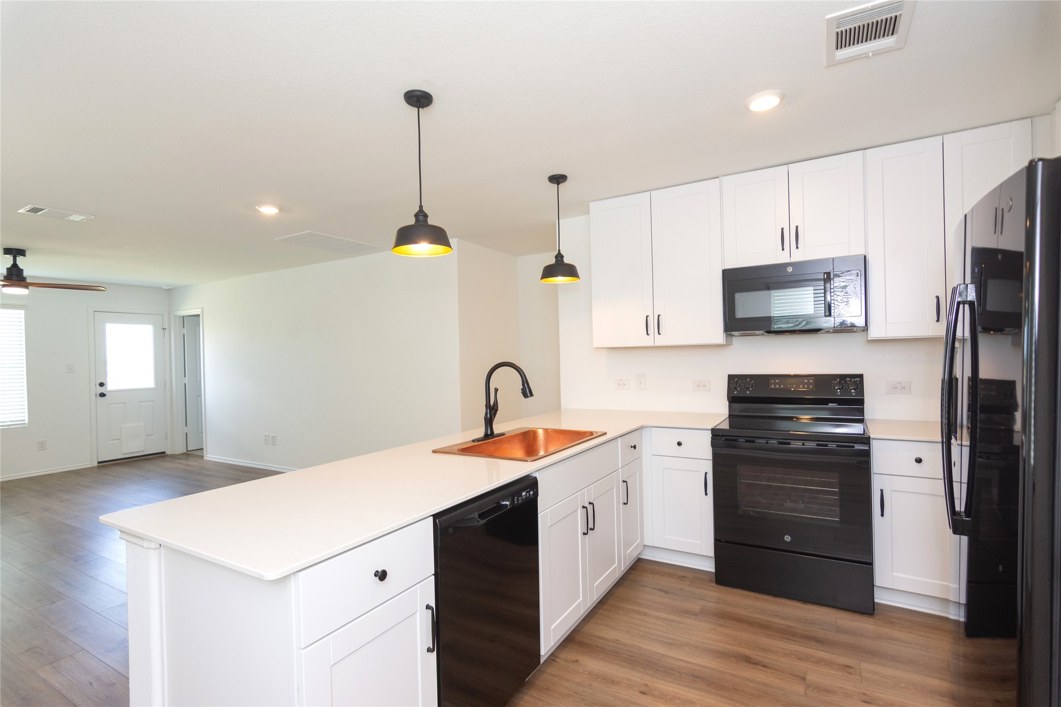 548 Rancho Del Cielo Loop Jarrell, TX 76537 - Photo 5 of 40 Modern kitchen featuring white shaker cabinetry, black appliances, a copper sink, and wood-finish flooring
