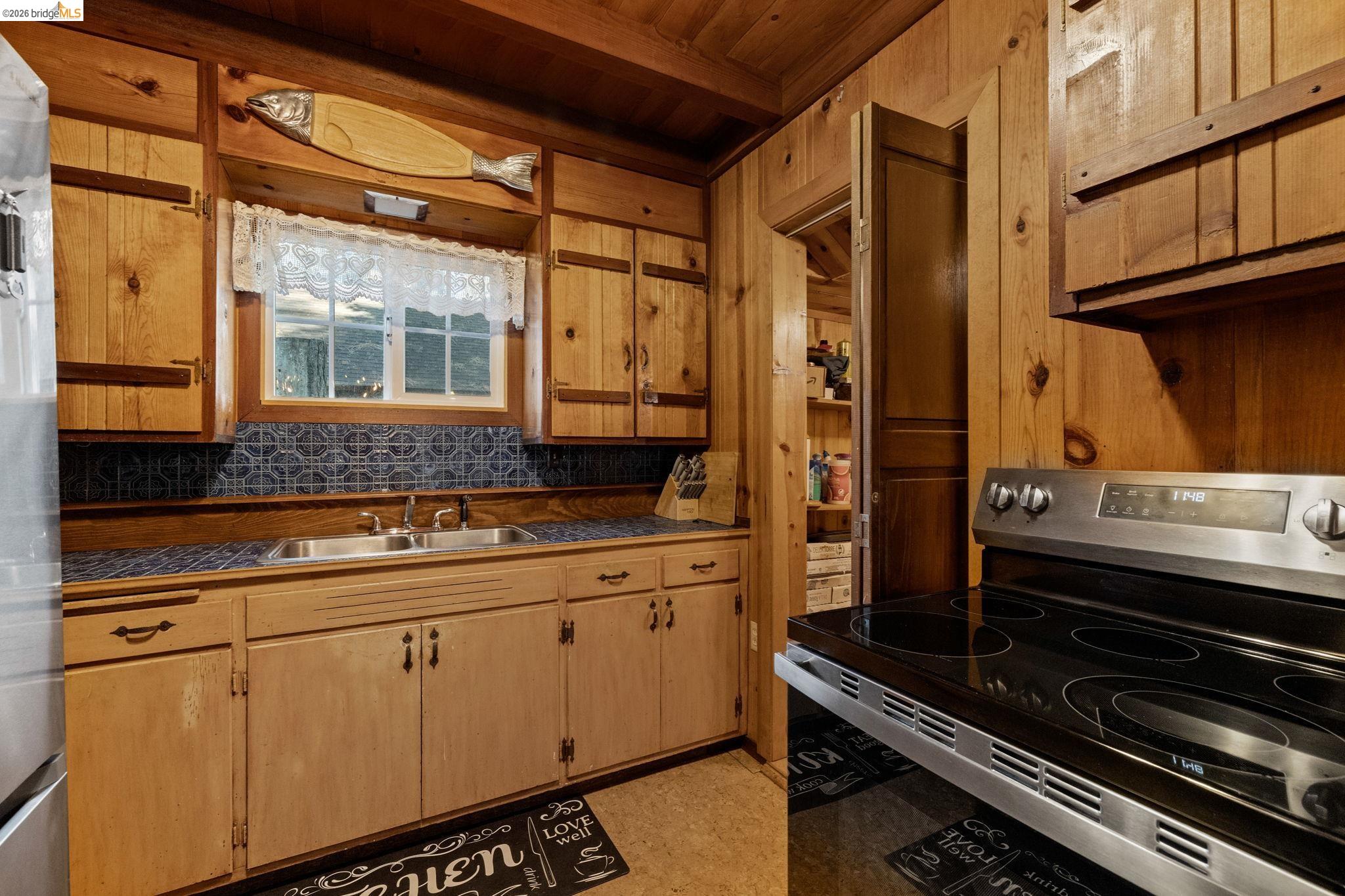26175 Janice Way Long Barn, CA 95335 - Photo 8 of 23 Kitchen featuring stainless steel appliances, a wood ceiling with exposed beams, dark countertops, wood walls, and light wood finish cabinets
