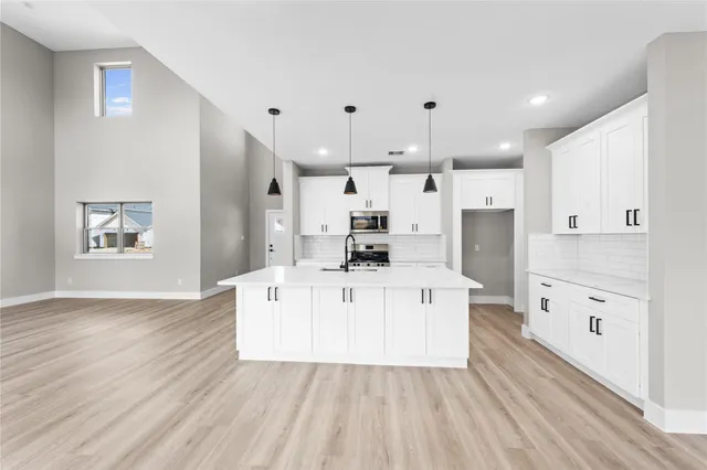 a large white kitchen with kitchen island a refrigerator a stove a sink dishwasher and white cabinets with wooden floor