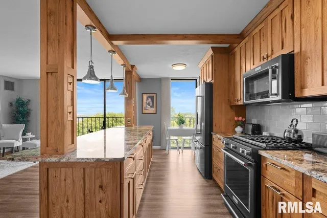 a kitchen with stainless steel appliances granite countertop a refrigerator a stove top oven and a sink with wooden floor