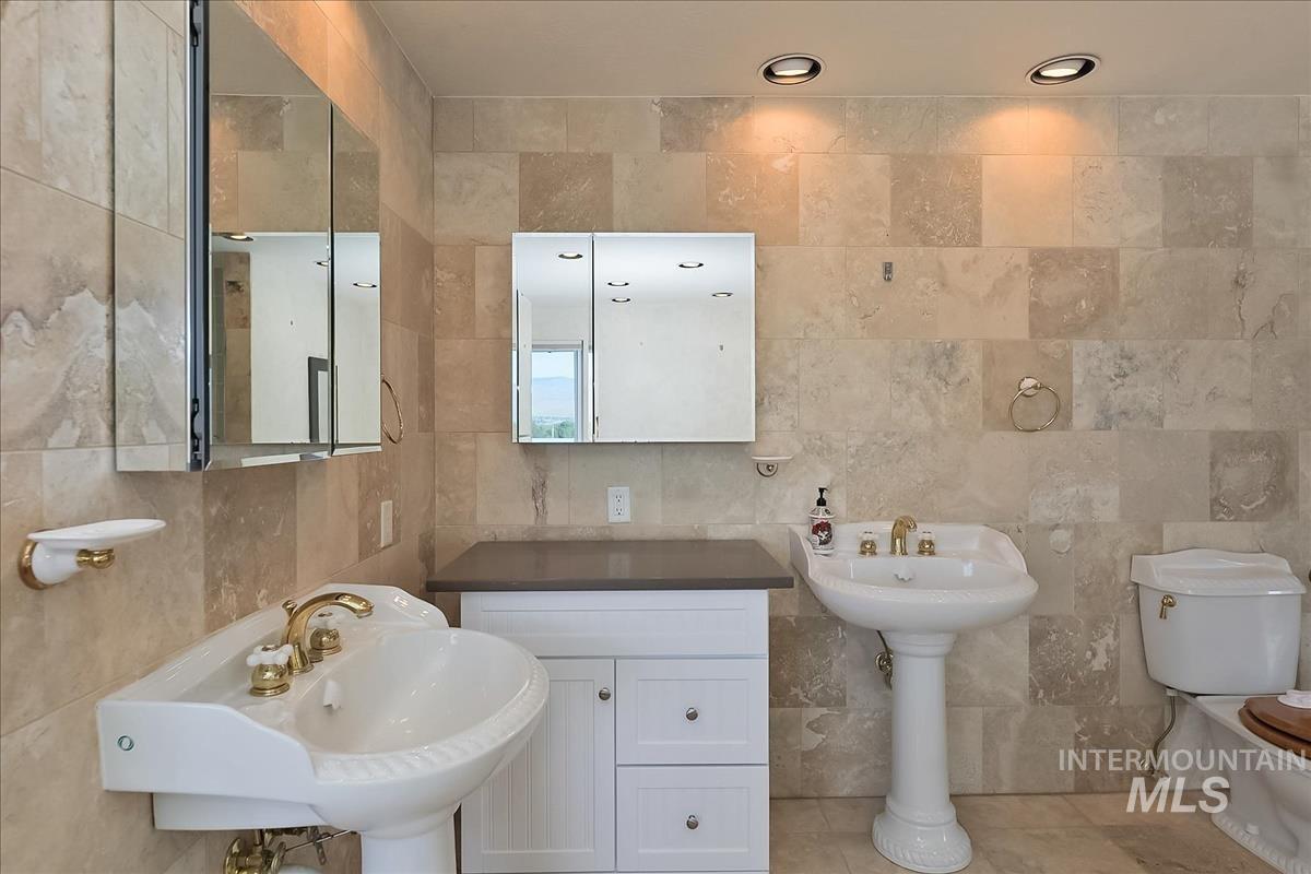 2804 West Sunrise Rim Road Boise, ID 83705 - Photo 39 of 50 Bathroom featuring full wall and floor tiling, two white porcelain pedestal sinks with brass-finish fixtures, and recessed ceiling lighting