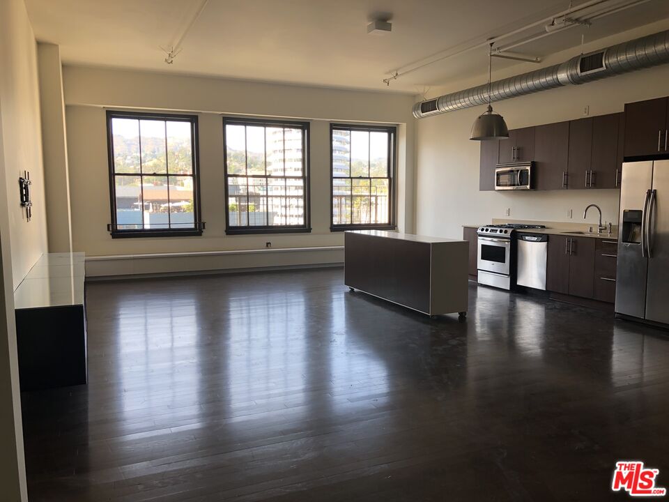 a living room with stainless steel appliances wooden floors and a view of kitchen