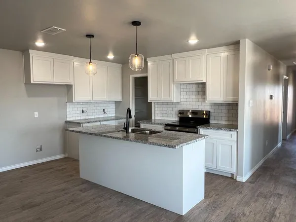 a kitchen with stainless steel appliances granite countertop a sink a stove a refrigerator and white cabinets