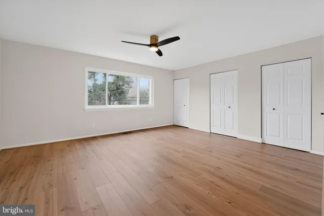 an empty room with wooden floor a ceiling fan and windows