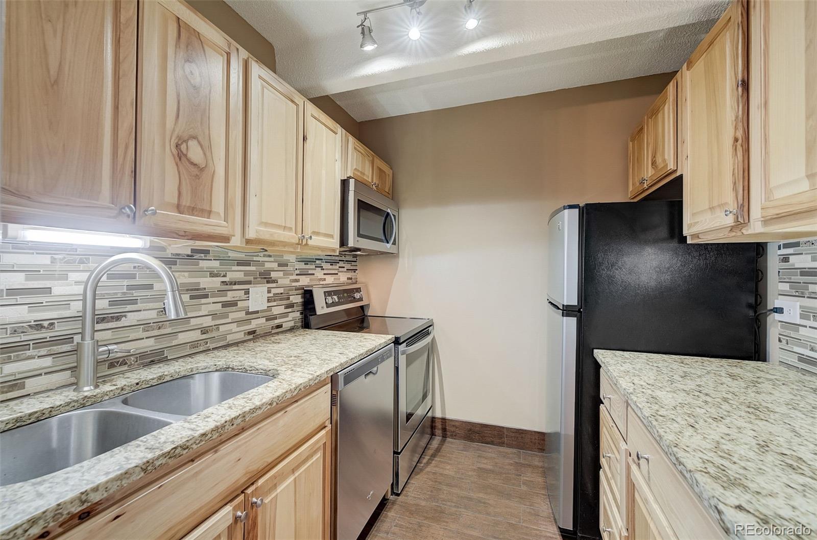a kitchen with stainless steel appliances granite countertop a sink a stove and a refrigerator with wooden cabinets