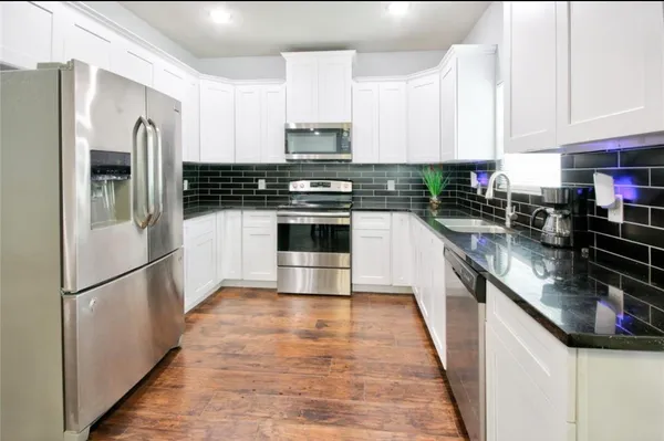 a kitchen with stainless steel appliances granite countertop a refrigerator a stove a sink and white cabinets