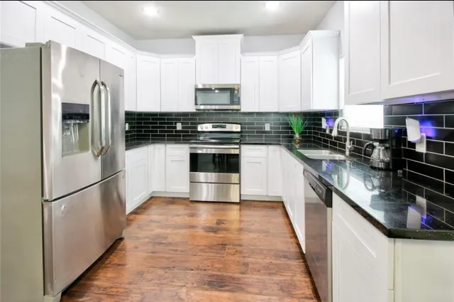 a kitchen with stainless steel appliances granite countertop a refrigerator a stove a sink and white cabinets