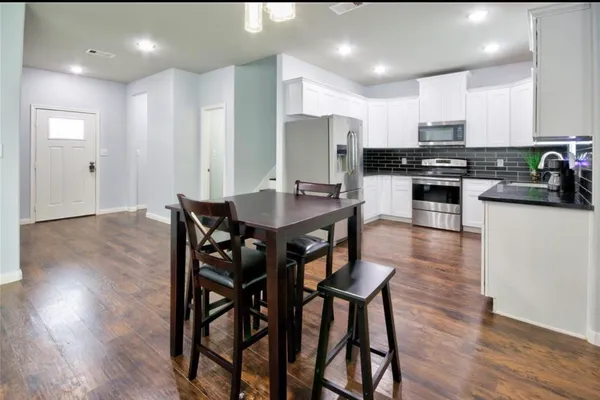 a kitchen with stainless steel appliances kitchen island granite countertop wooden floor refrigerator and dining table