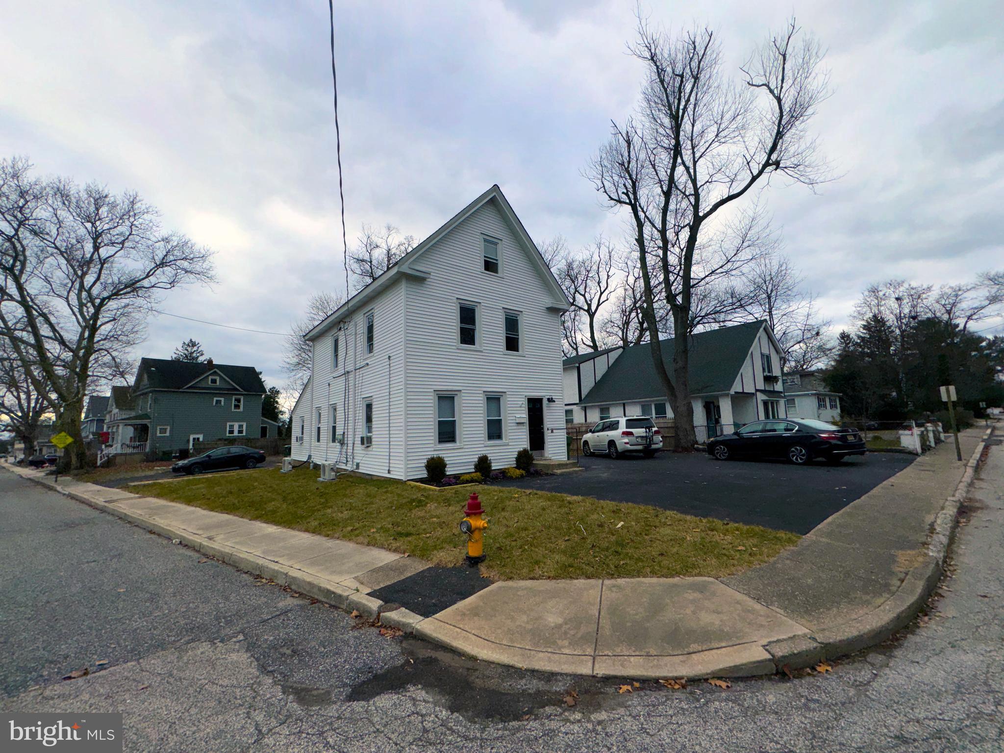 a view of a white house next to a yard with big trees