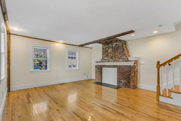 a view of an empty room with wooden floor fireplace and a window