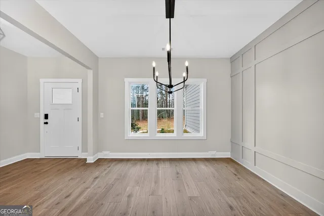 a view of an empty room with wooden floor kitchen view and a window