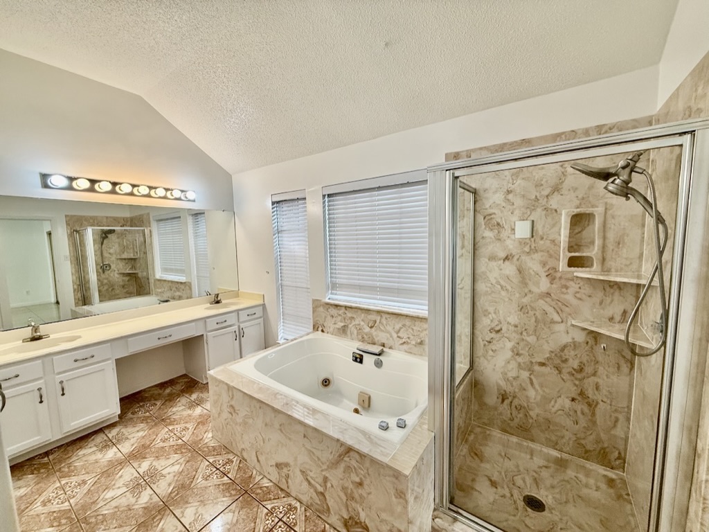 604 Cactus Bend Drive Pflugerville, TX 78660 - Photo 18 of 29 Full bath with double vanity, a stall shower, lofted ceiling, a jetted tub, and a textured ceiling