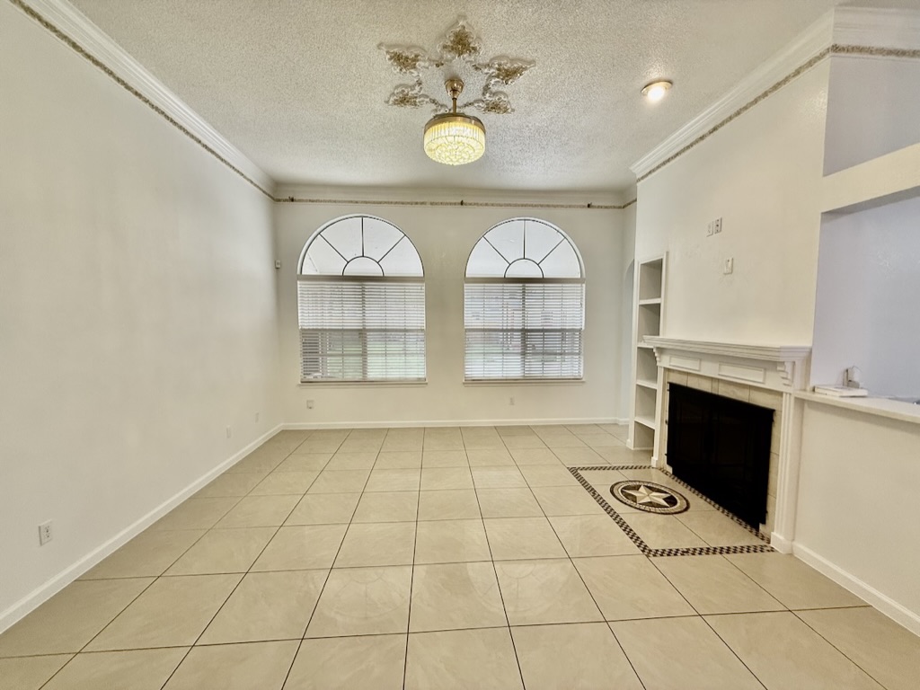 604 Cactus Bend Drive Pflugerville, TX 78660 - Photo 7 of 29 Unfurnished living room featuring built in shelves, a tile fireplace, tile patterned flooring, and crown molding