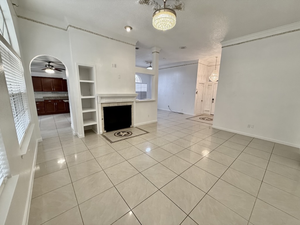 604 Cactus Bend Drive Pflugerville, TX 78660 - Photo 8 of 29 Unfurnished living room with built in features, light tile patterned floors, a textured ceiling, baseboards, and ceiling fan with notable chandelier
