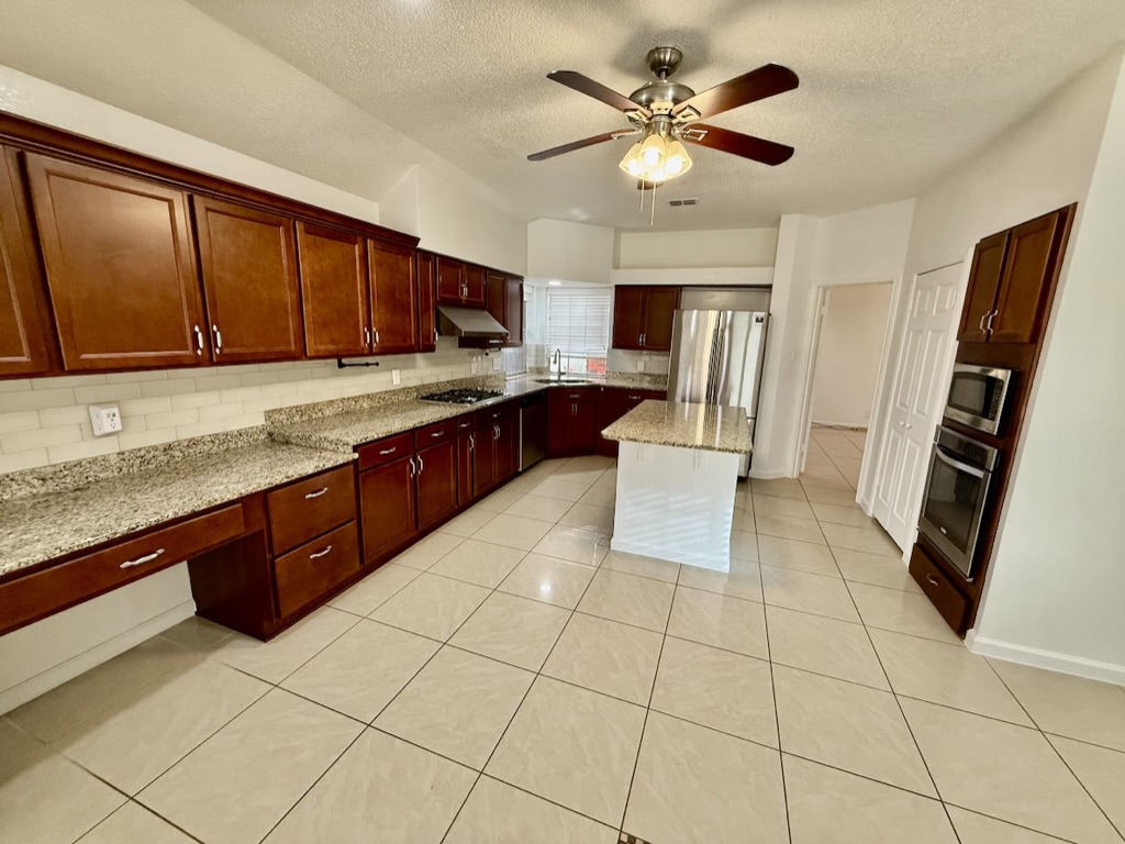 604 Cactus Bend Drive Pflugerville, TX 78660 - Photo 9 of 29 Kitchen with light tile patterned floors, tasteful backsplash, a ceiling fan, a center island, and stainless steel appliances