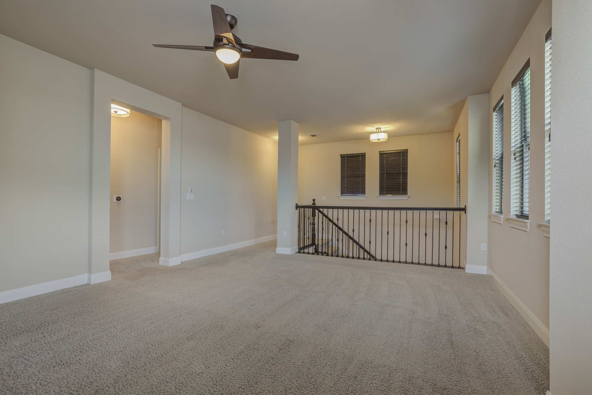 4524 Berkman Drive Austin, TX 78723 - Photo 27 of 38 Carpeted loft space featuring multiple windows with blinds, a ceiling fan with integrated lighting, recessed lighting, and a dark iron railing overlooking a lower level