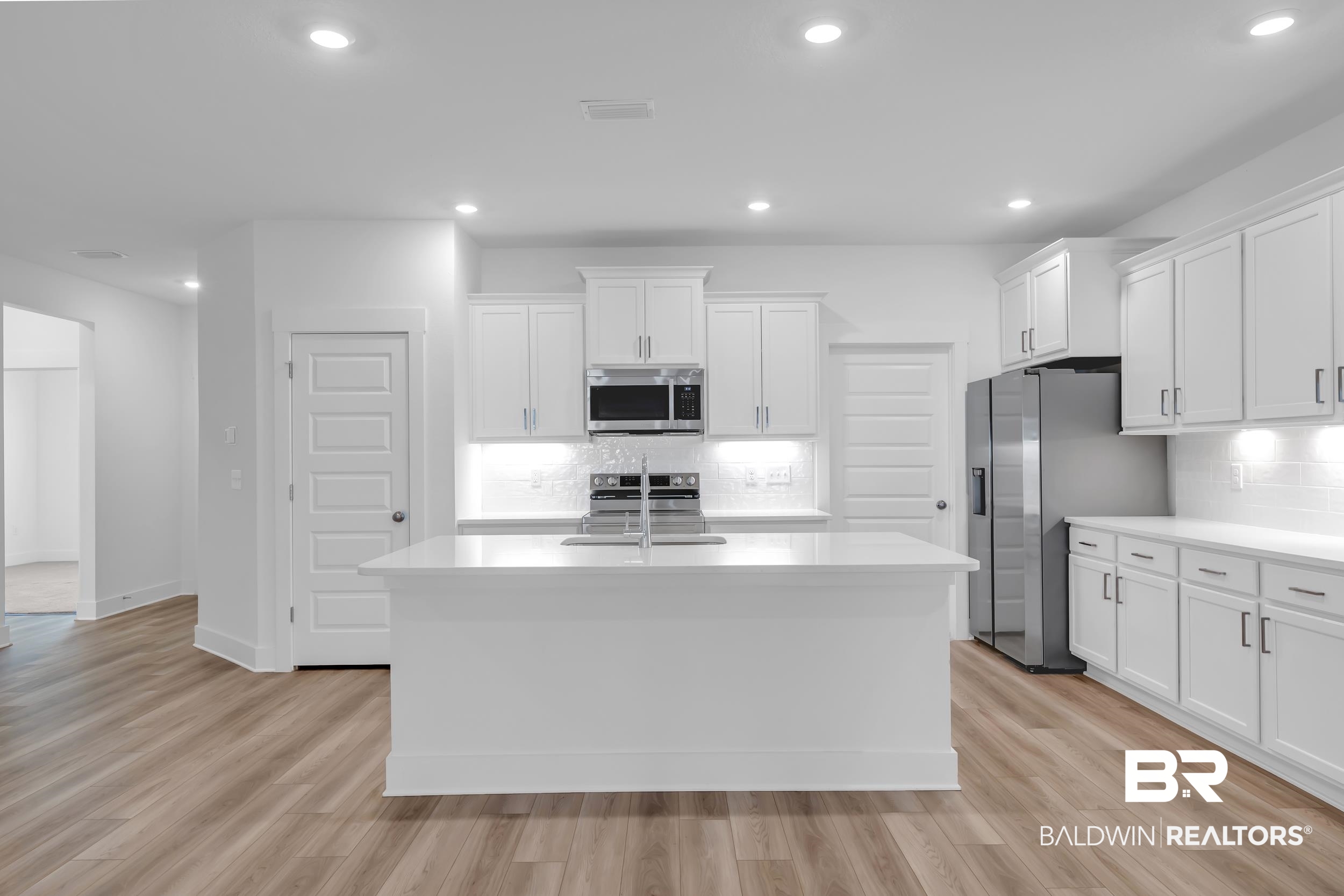 9933 Weller Cove Foley, AL 36535 - Photo 12 of 36 Kitchen featuring a central island with an undermount sink, white cabinetry, integrated stainless steel appliances, white subway tile backsplash, and wood-finish flooring