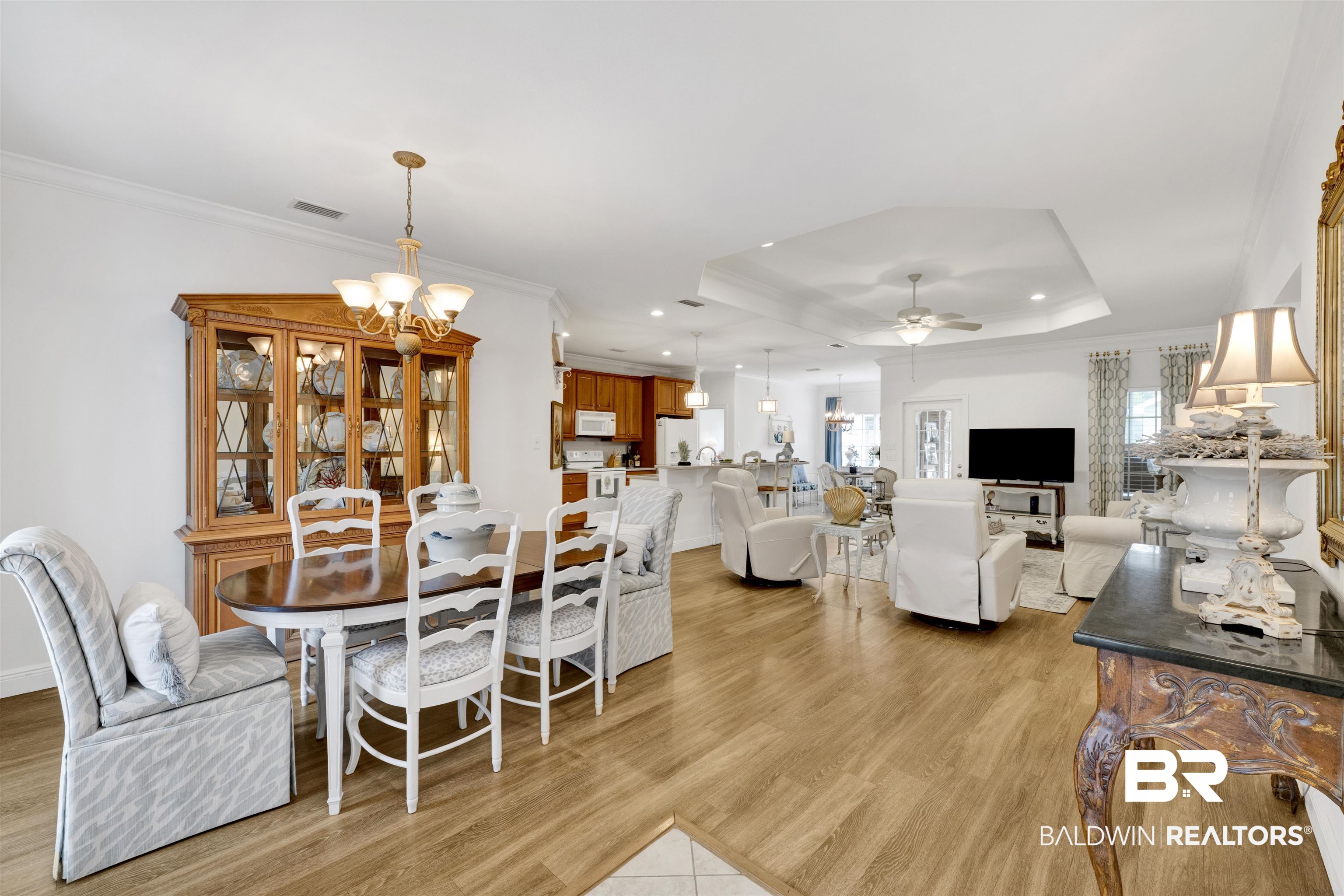 Dining space featuring crown molding, a ceiling fan, a chandelier, light wood-style flooring, and a raised ceiling