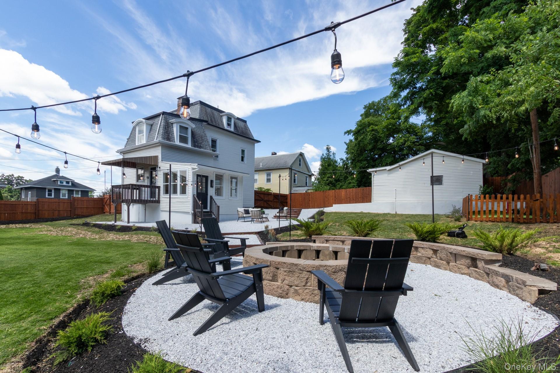 114 Rombout Avenue Beacon, NY 12508 - Photo 32 of 32 Backyard fire pit area with gravel ground cover, stone block retaining wall, and string lighting