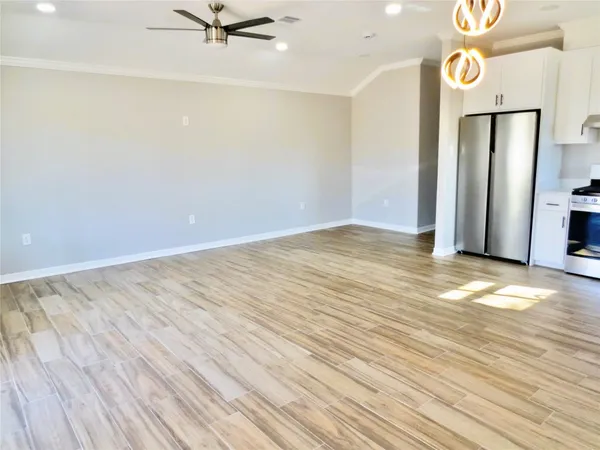 a view of an empty room with wooden floor and a ceiling fan