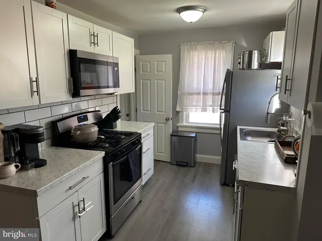 a kitchen with stainless steel appliances a sink dishwasher a stove top oven a refrigerator with wooden floor and cabinets