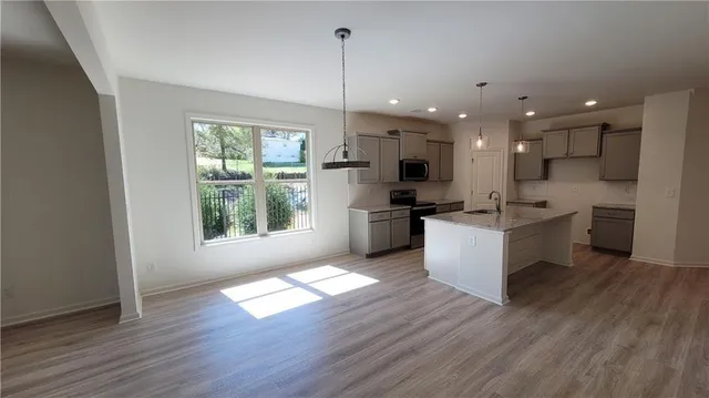 a kitchen with stainless steel appliances kitchen island granite countertop a stove a sink a refrigerator and white cabinets with wooden floor