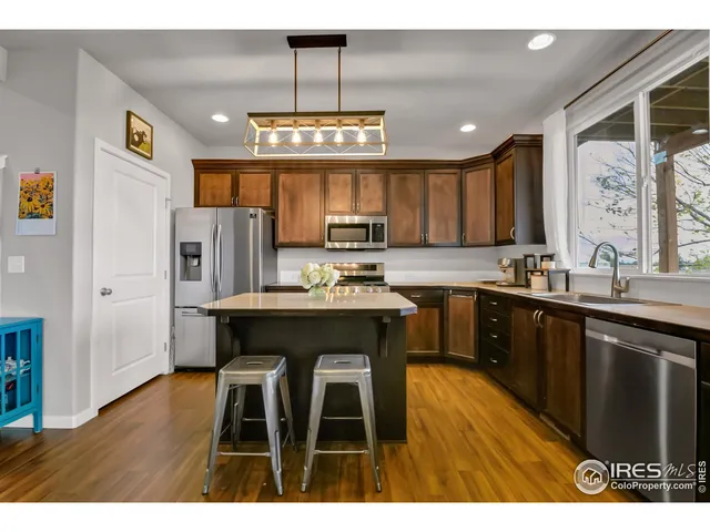 a kitchen with stainless steel appliances granite countertop a refrigerator a sink dishwasher a stove and a dining table with wooden floor