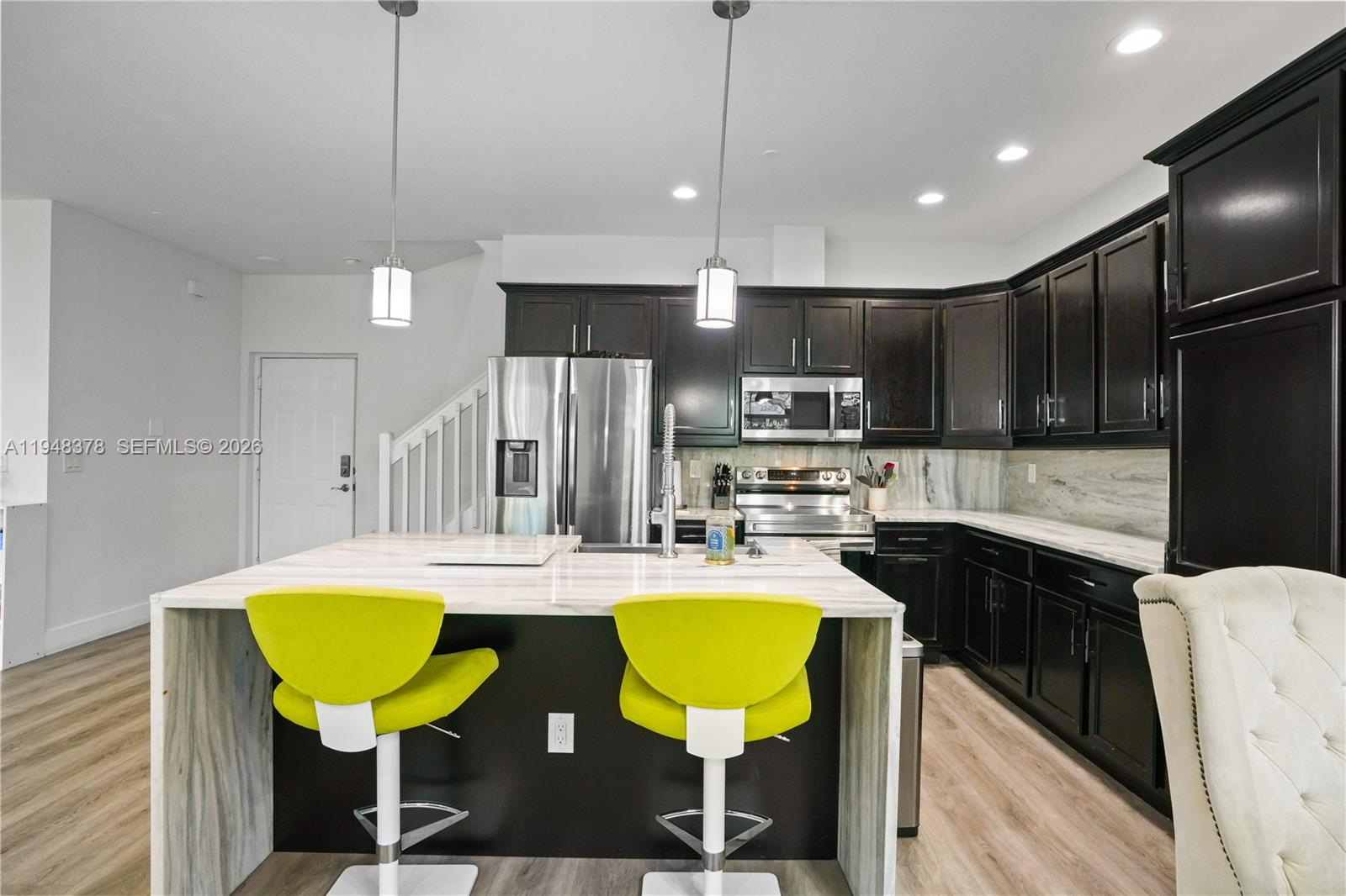 2913 Cascada Isle Way Cooper City, FL 33024 - Photo 10 of 50 a kitchen with stainless steel appliances granite countertop a sink a stove a refrigerator cabinets and chairs with wooden floor