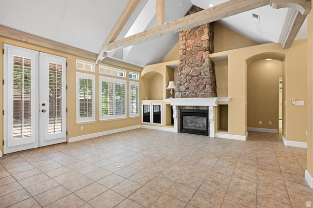 20 Valley Road Leeds, UT 84746 - Photo 11 of 57 Vaulted ceiling with exposed wood beams, featuring a stone fireplace with a white mantel, built-in shelving, French doors with louvered shutters, and tile flooring