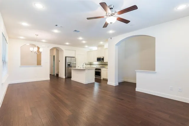 a view of an empty room and kitchen with wooden floor