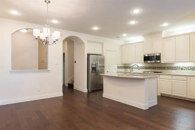 a kitchen with stainless steel appliances granite countertop a refrigerator a sink dishwasher a stove and white cabinets with wooden floor