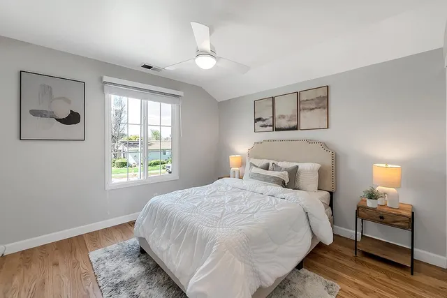 a bedroom with a bed and a lamp on dresser with wooden floor
