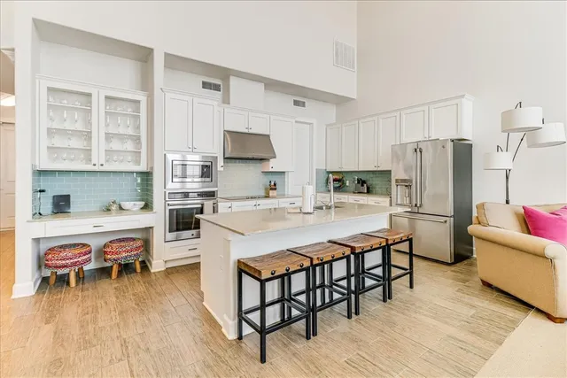 a kitchen with stainless steel appliances a stove a sink a refrigerator and a dining table with wooden floor