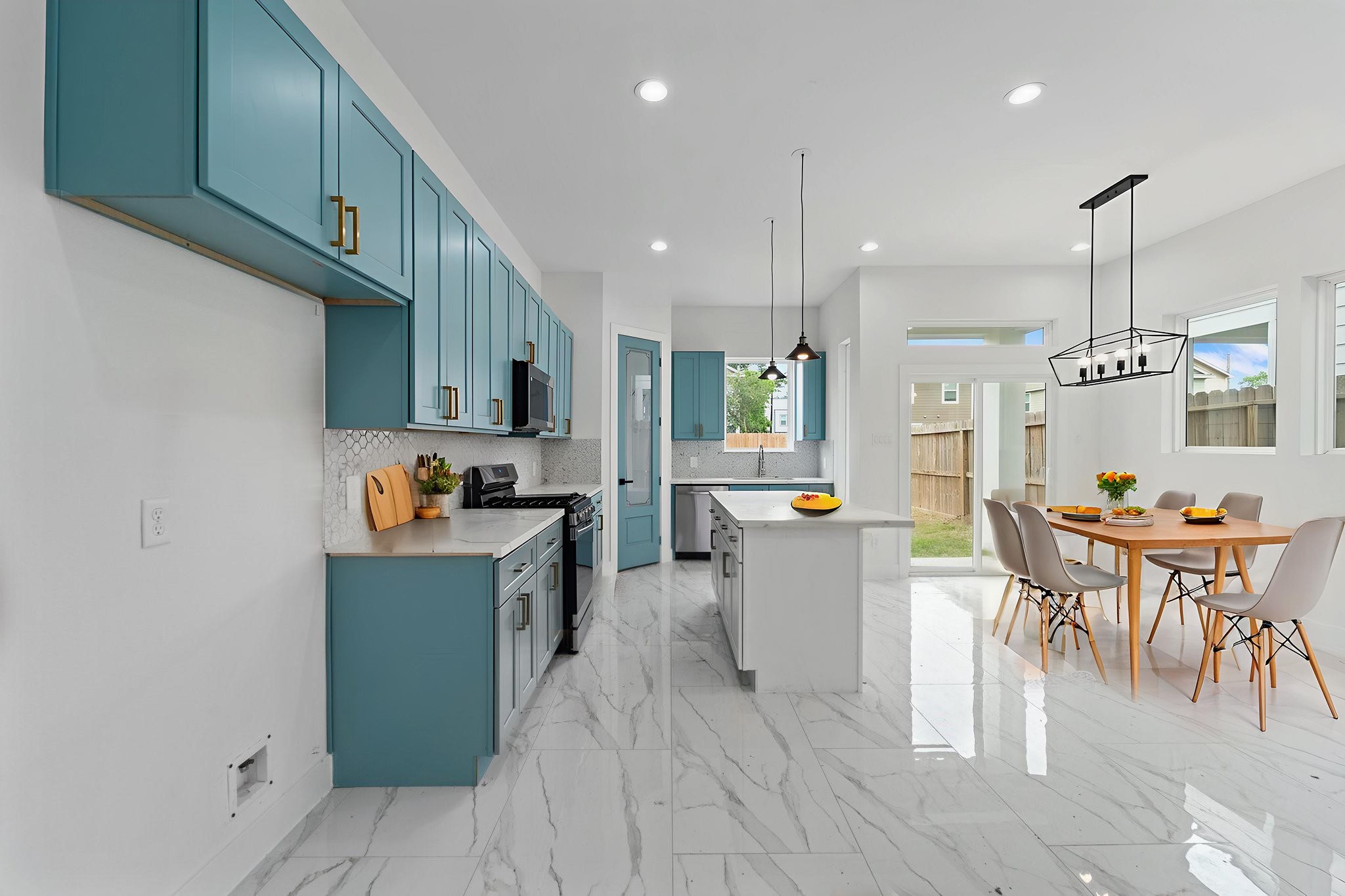 7709 Willow Street Houston, TX 77088 - Photo 5 of 15 Modern open-concept kitchen and dining area featuring vibrant blue cabinetry, elegant gold-tone accents, and sleek marble-style flooring.