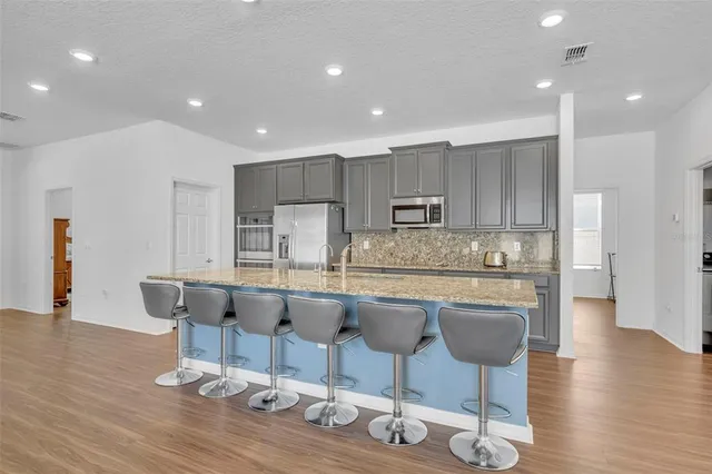 a kitchen with stainless steel appliances granite countertop a stove top oven a sink dishwasher a dining table and chairs with wooden floor