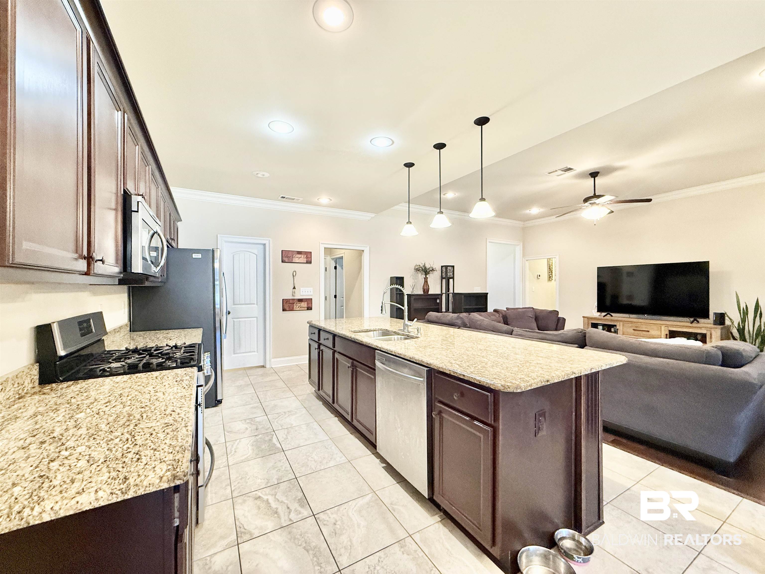 7011 Rocky Rd Loop Gulf Shores, AL 36542 - Photo 65 of 66 Kitchen featuring stainless steel appliances, crown molding, open floor plan, hanging light fixtures, and dark brown cabinetry
