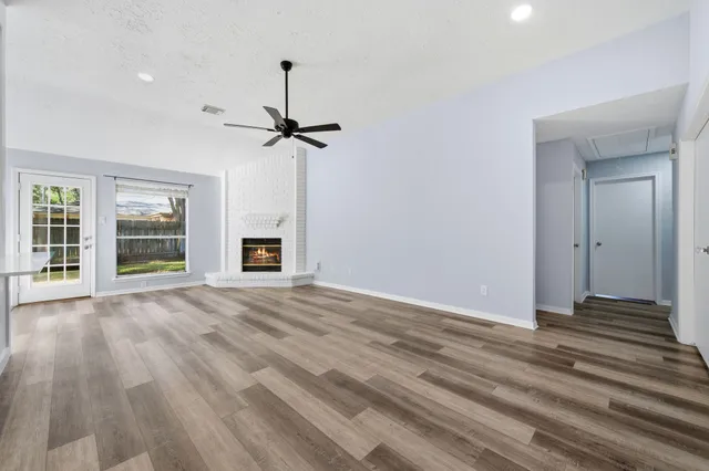 a view of an empty room with wooden floor fireplace and a window
