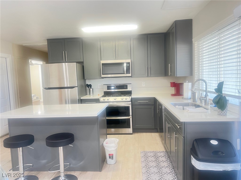 4194 Greenpoint Street Las Vegas, NV 89147 - Photo 7 of 25 Kitchen featuring appliances with stainless steel finishes, light stone counters, gray cabinets, and a kitchen breakfast bar