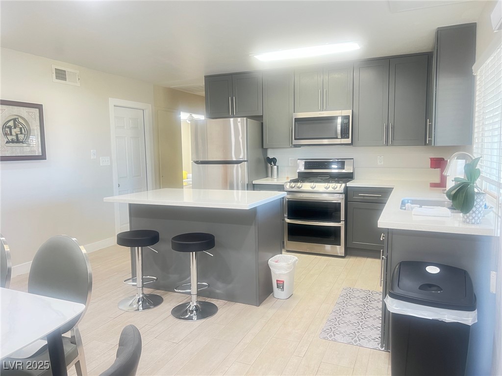 4194 Greenpoint Street Las Vegas, NV 89147 - Photo 9 of 25 Kitchen featuring appliances with stainless steel finishes, a kitchen island, a kitchen bar, gray cabinets, and light stone counters