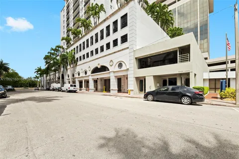 a front view of a building with lot of cars and trees