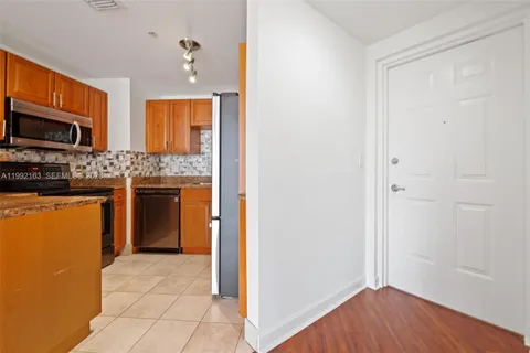 a view of empty room with wooden floor and kitchen